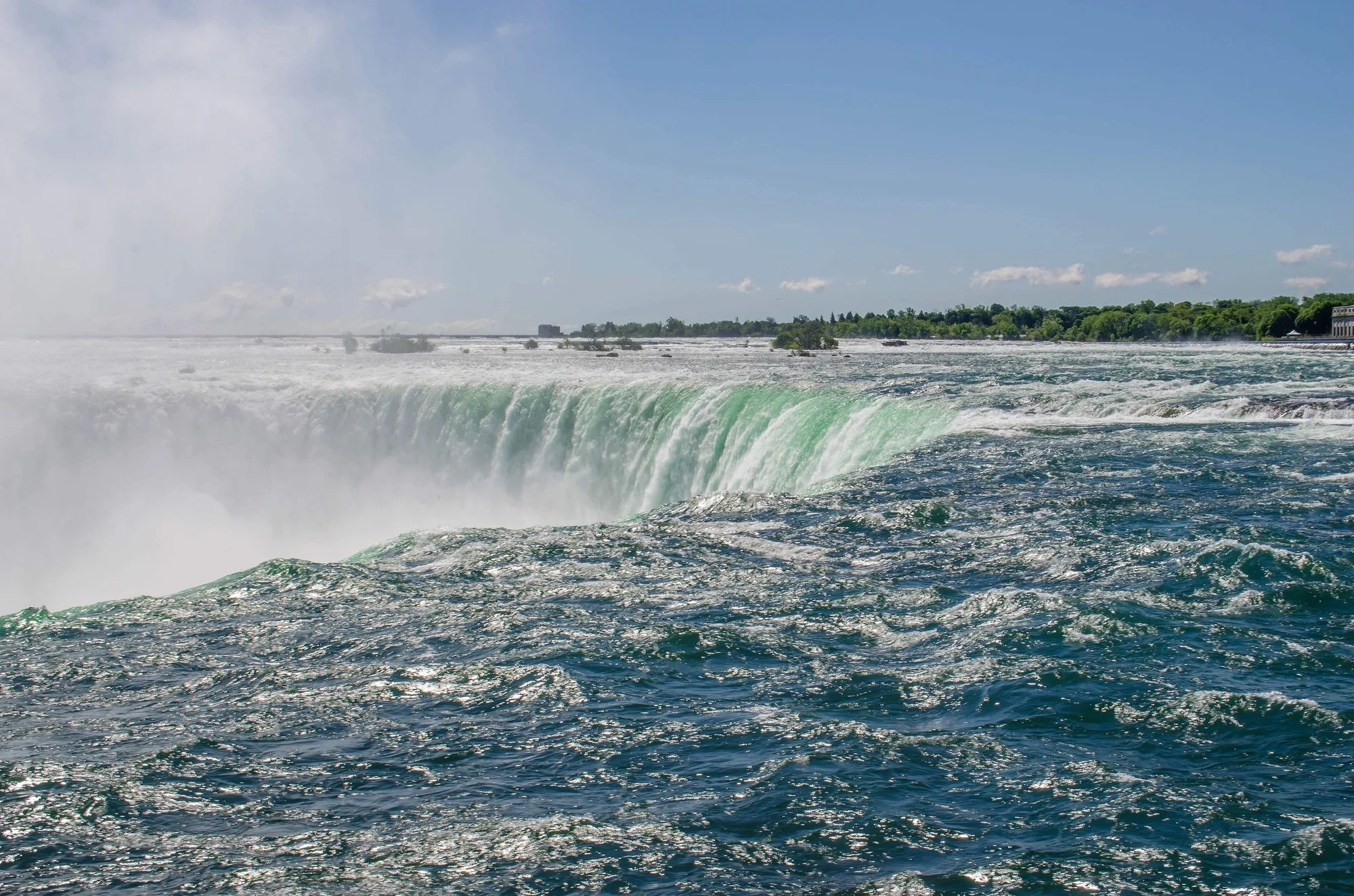 Green water curves over the broad Horseshoe Falls, with white mist rising above the falling water.