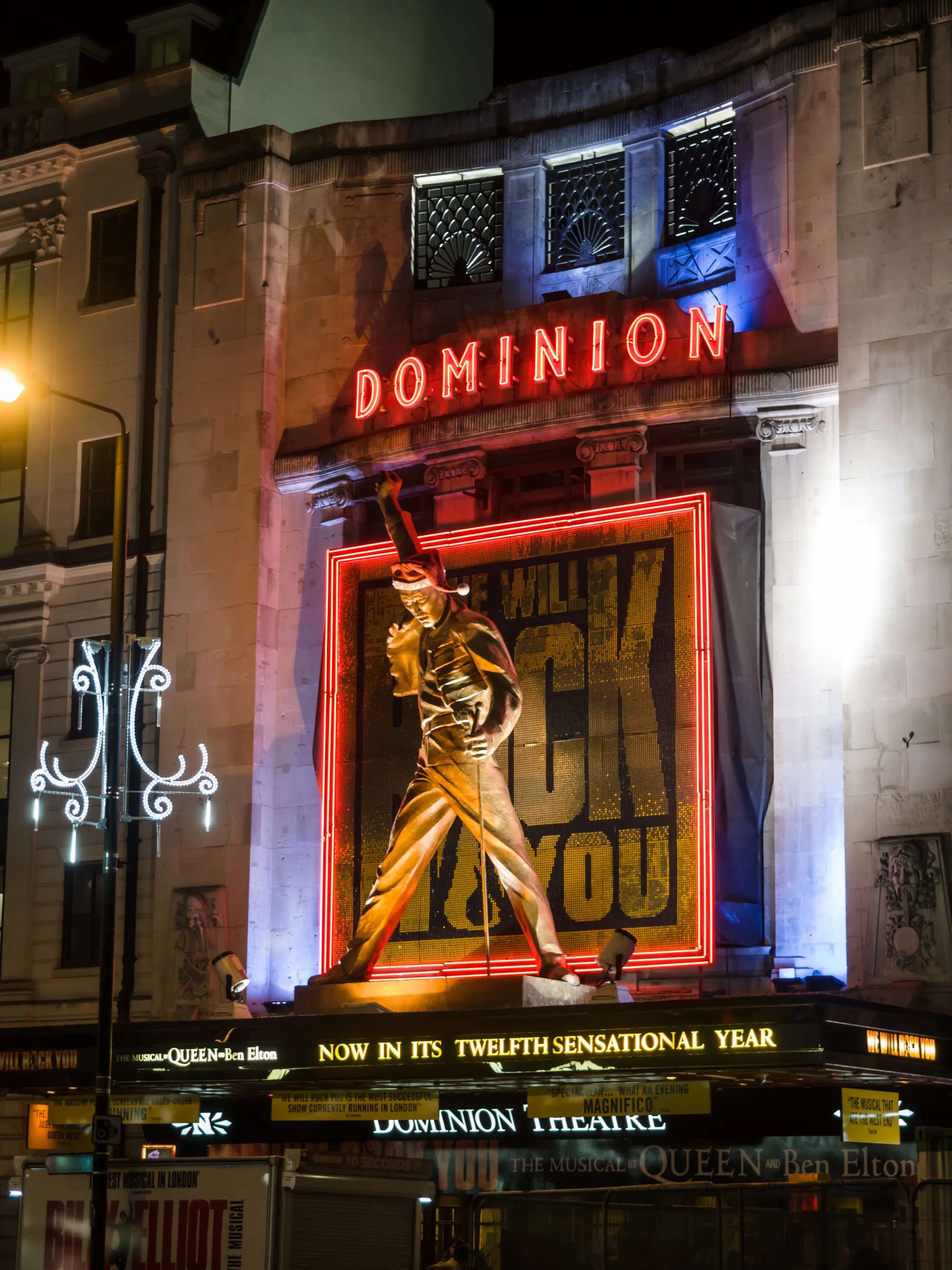 The front of the Dominion Theatre on Tottenham Court Road, with a large illuminated show sign above the entrance.