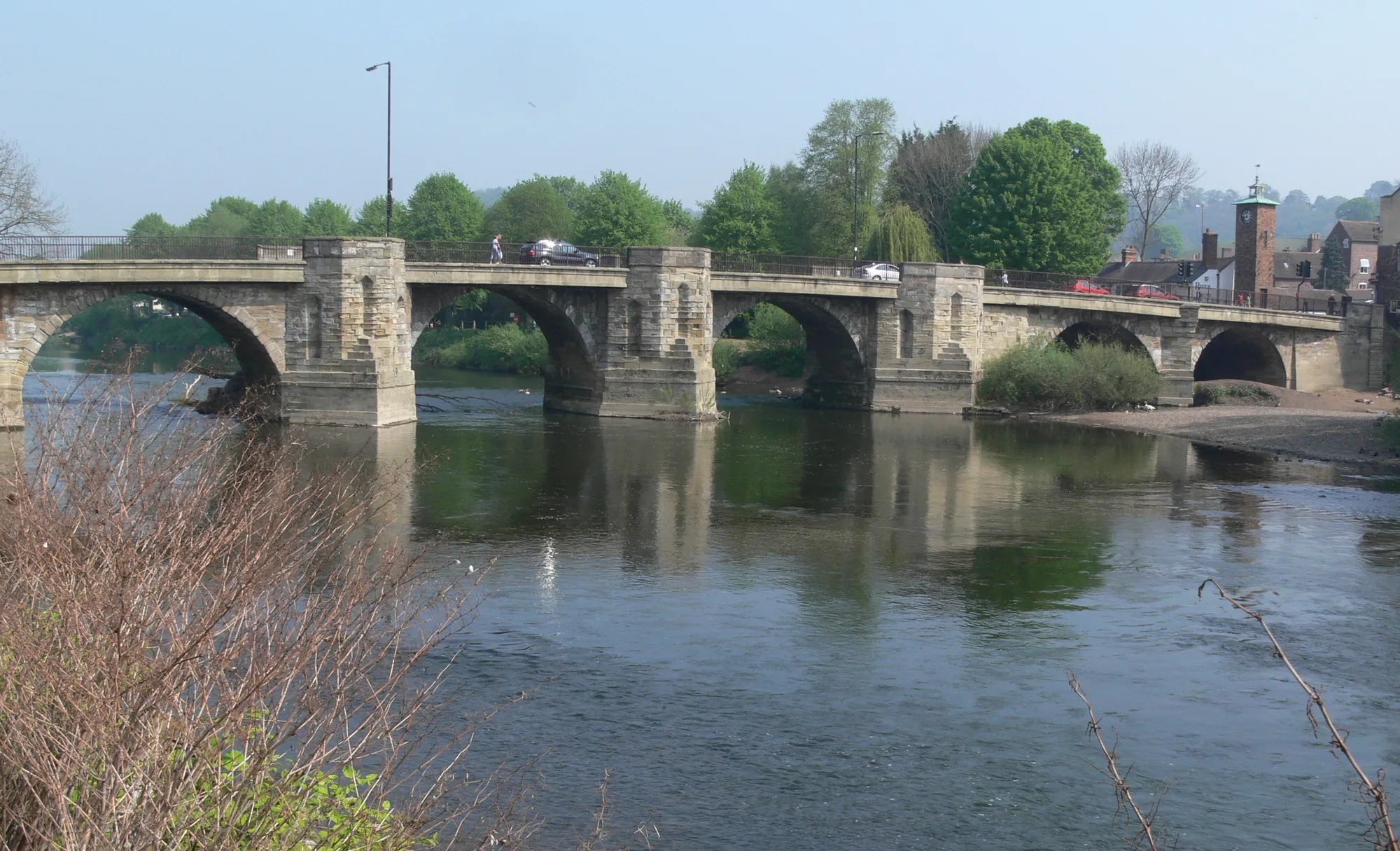 A stone bridge with several arches crossing the wide River Severn at Bridgnorth, with houses climbing the bank behind it.