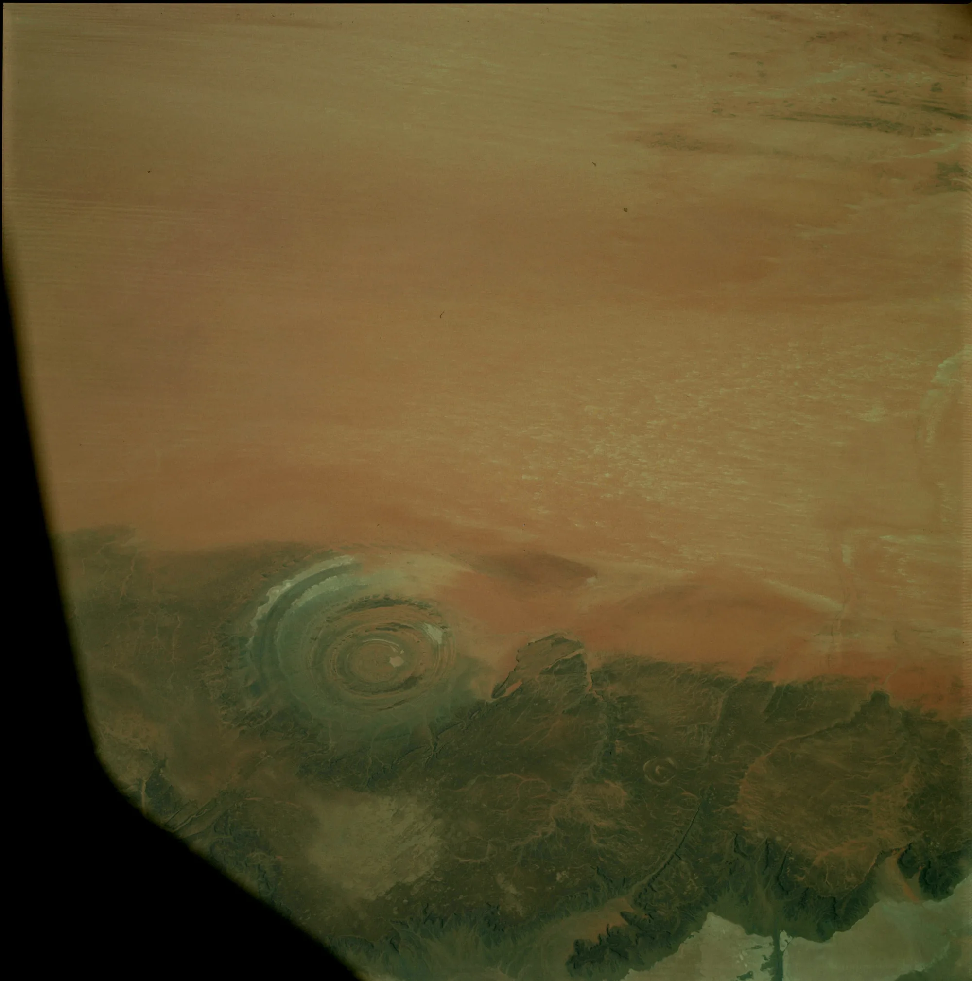A nearly circular banded formation appears beside dark ridges in a brown orbital photograph with a black border.